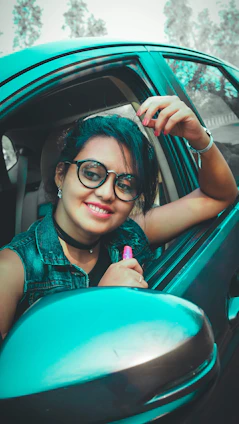 A smiling woman driver holding a pink kit bag inside her car, with city streets visible through the window.