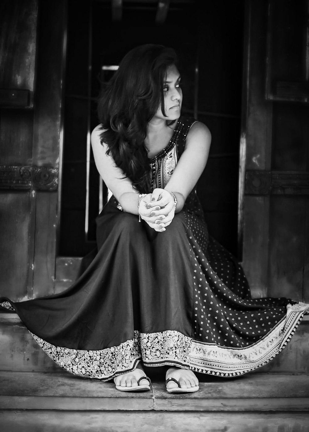 grayscale phot of woman wearing dress sitting besides door