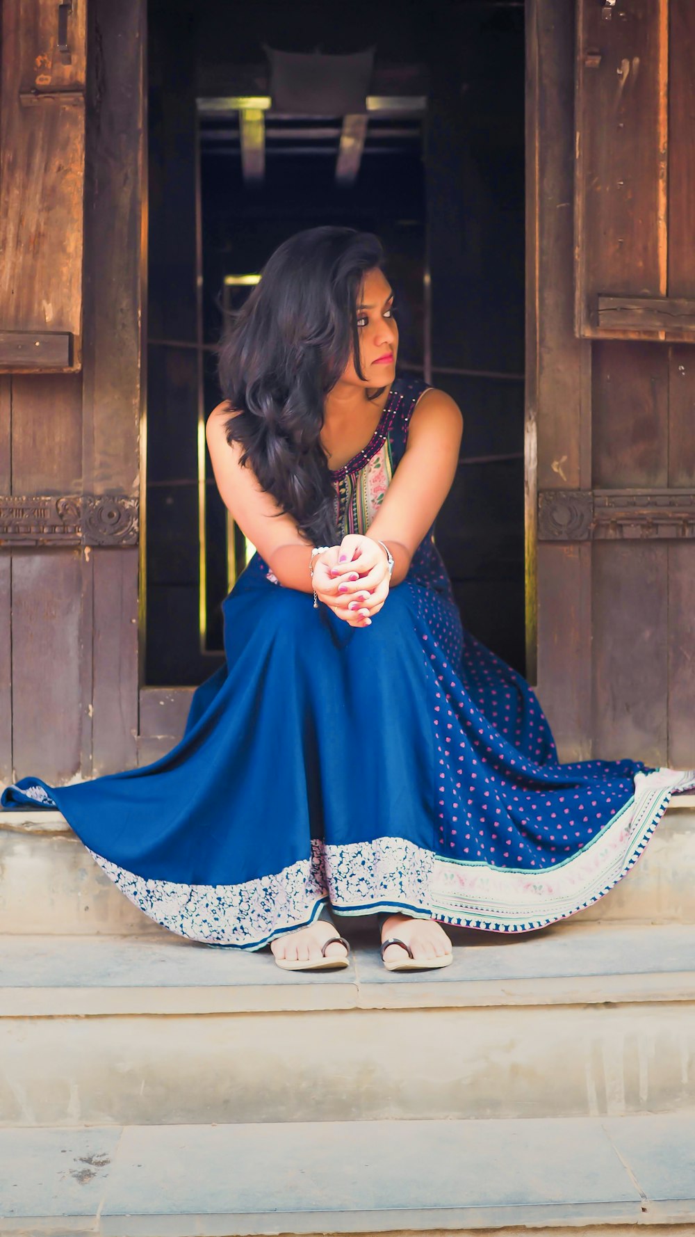 woman in blue and white polka-dot sleeveless dress sitting on stairs