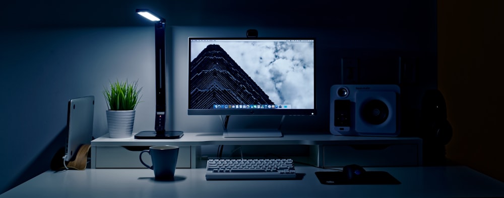 flat screen TV turned-on near keyboard, multimedia speaker, and ceramic mug on table