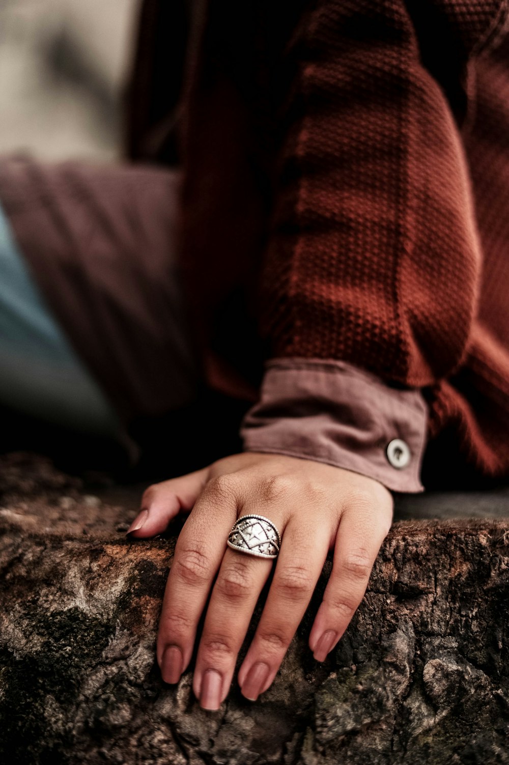 person sitting on brown tree trunk wearing silver-colored ring close-up photography