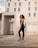 Confident woman stretching outdoors wearing sleek, minimalist activewear in a modern urban setting.