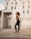 Confident woman stretching outdoors wearing sleek, minimalist activewear in a modern urban setting.