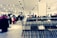 A clothing store interior featuring rows of metal clothing racks filled with hangers. The background is softly blurred, showcasing more clothing displays and bright ceiling lights, creating a spacious and modern retail environment.