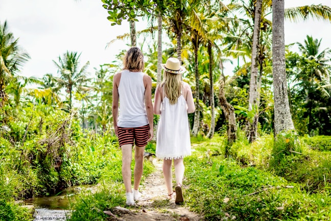 Couple walking along a quiet beach path surrounded by lush greenery.