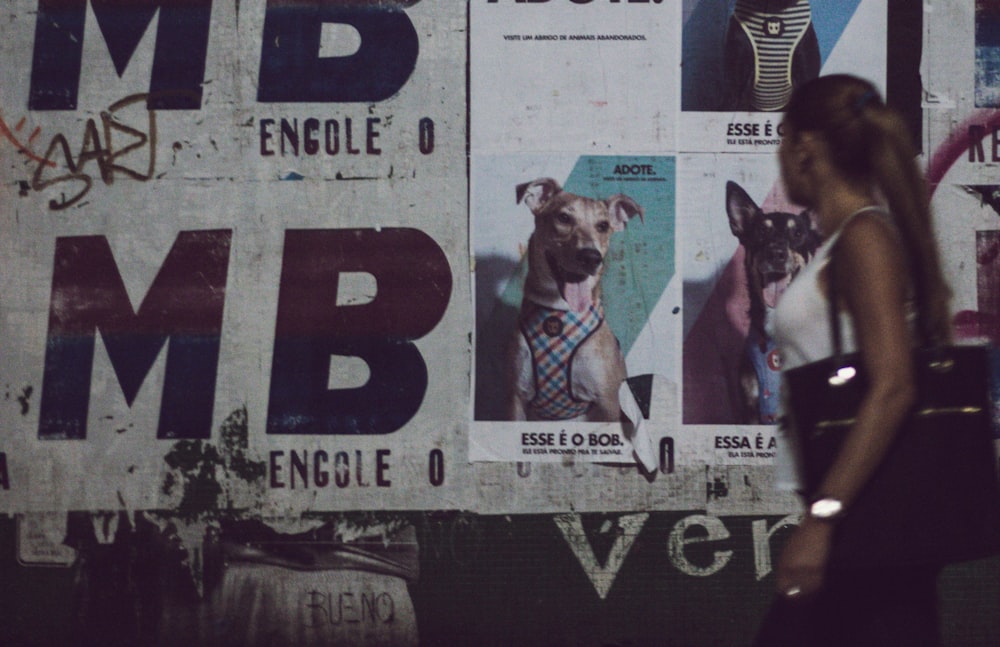 a woman walking past a wall covered in posters