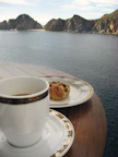 Close-up of a wooden deck with a steaming cup of coffee overlooking the canyon at sunrise.