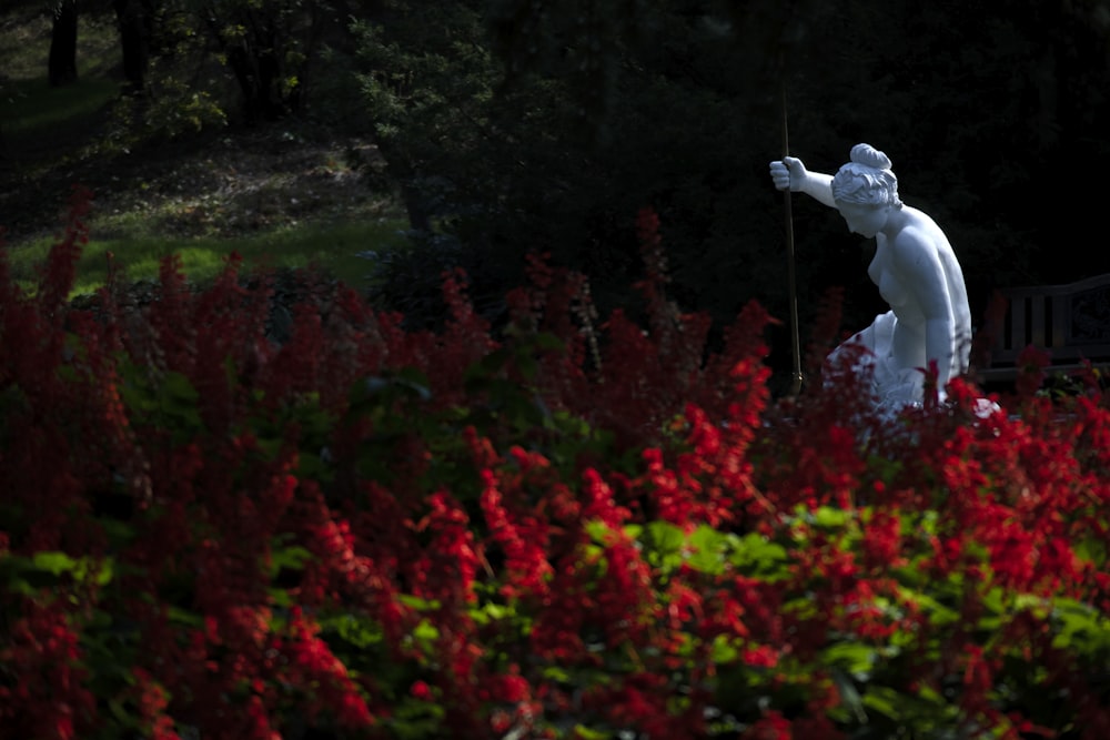 nude woman statue in garden with red blooming flowers