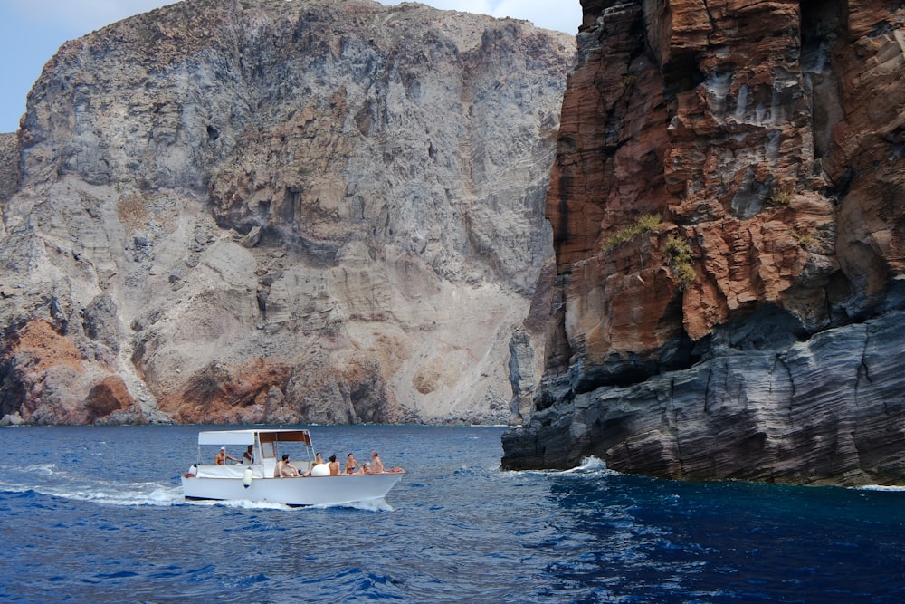 people in boat on body of water near brown rock mountains