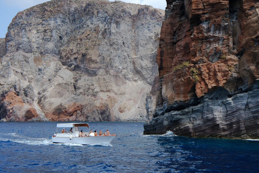 People aboard a small boat passing tall rocky coastal cliffs