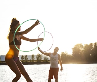 man and woman playing hula hoop near body of water