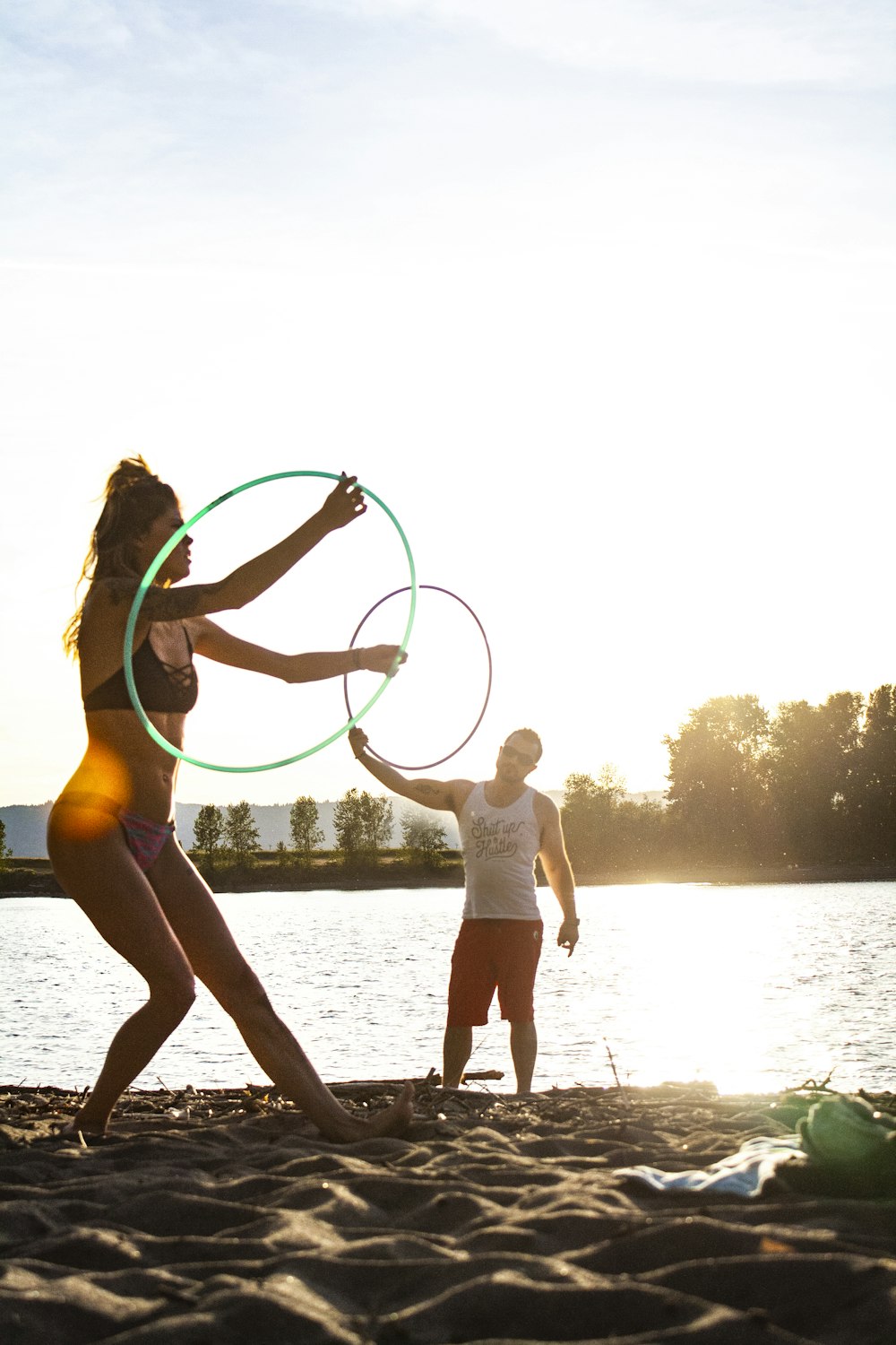 man and woman playing hula hoop near body of water