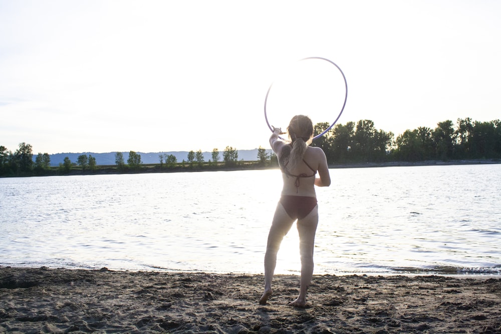 woman wearing brown bikini holding hula hoop standing on seashore