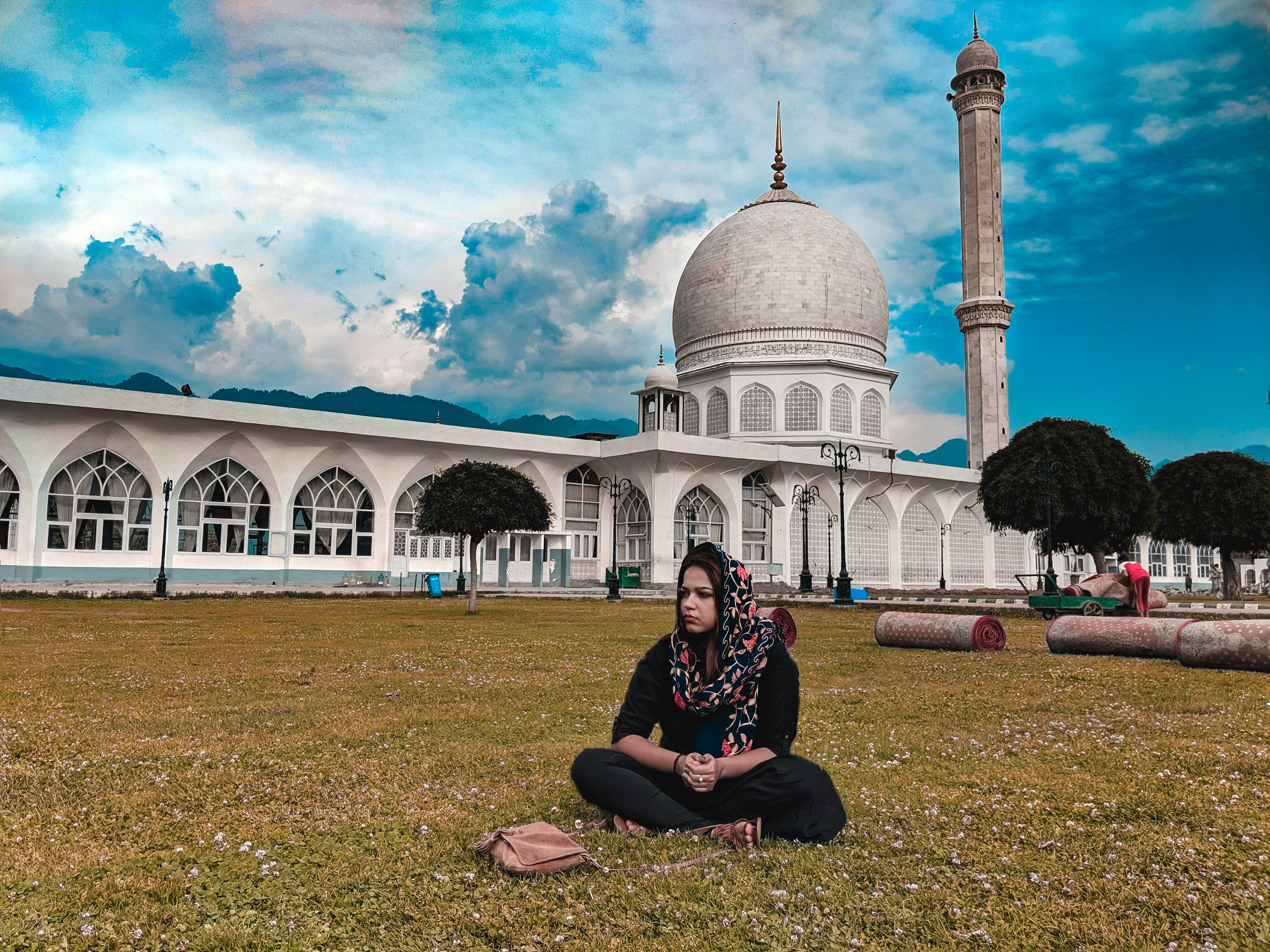 Wanita mengenakan jilbab abu-abu duduk di depan gedung kubah