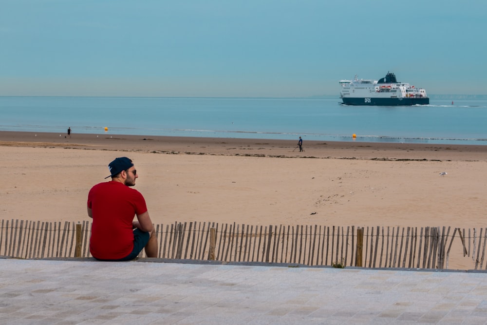 man wearing red shirt sitting on seashore