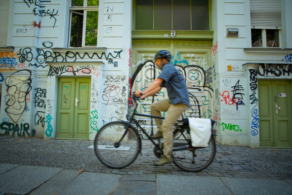 man riding bicycle beside graffiti building