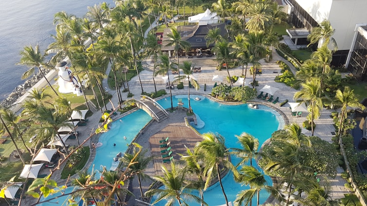 Sunlit view of the villa’s lagoon-style pool surrounded by lush palm trees and comfortable lounge chairs, with children playing safely in the shallow water.