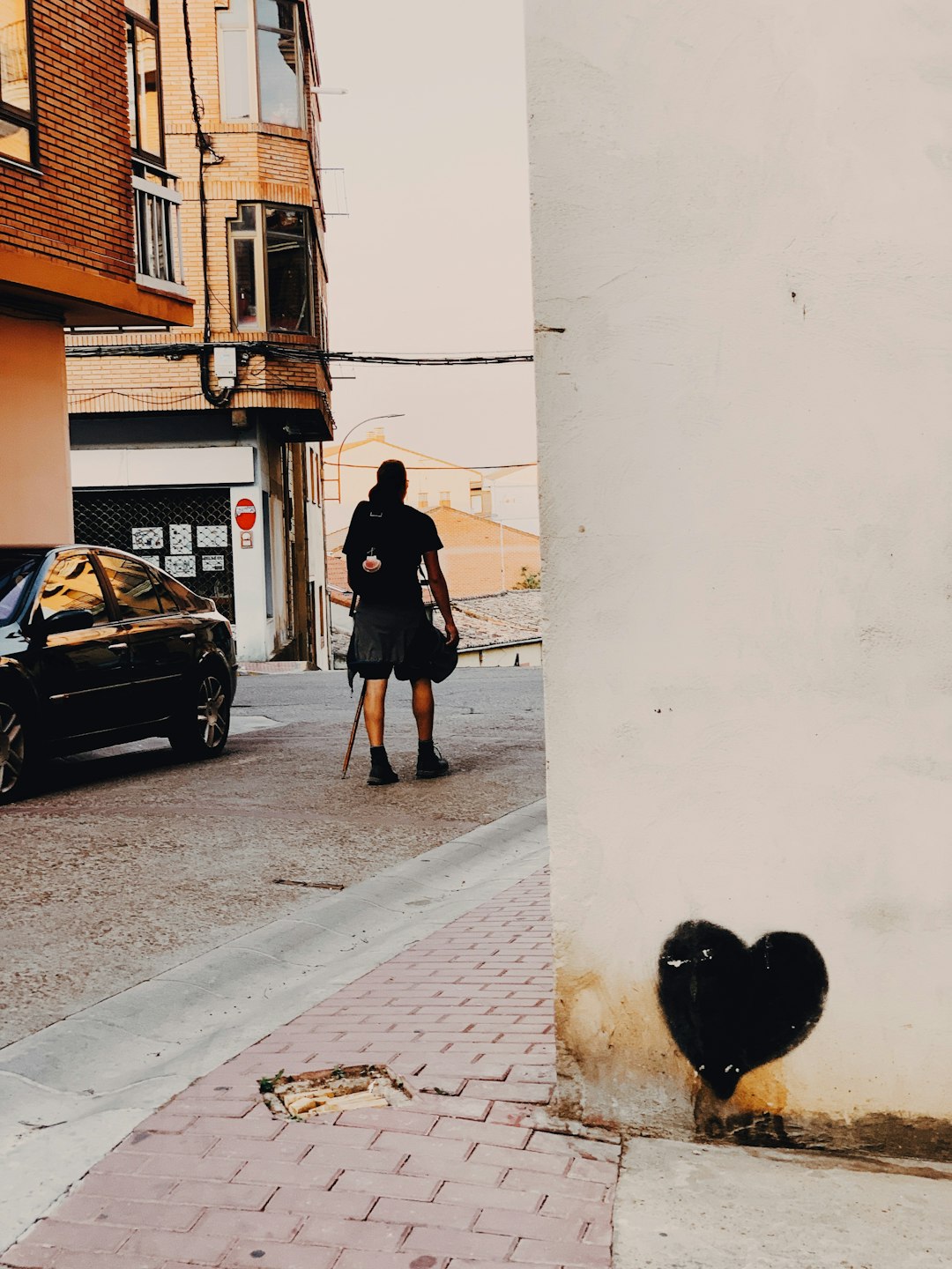 man walking on road passes by black car during daytime