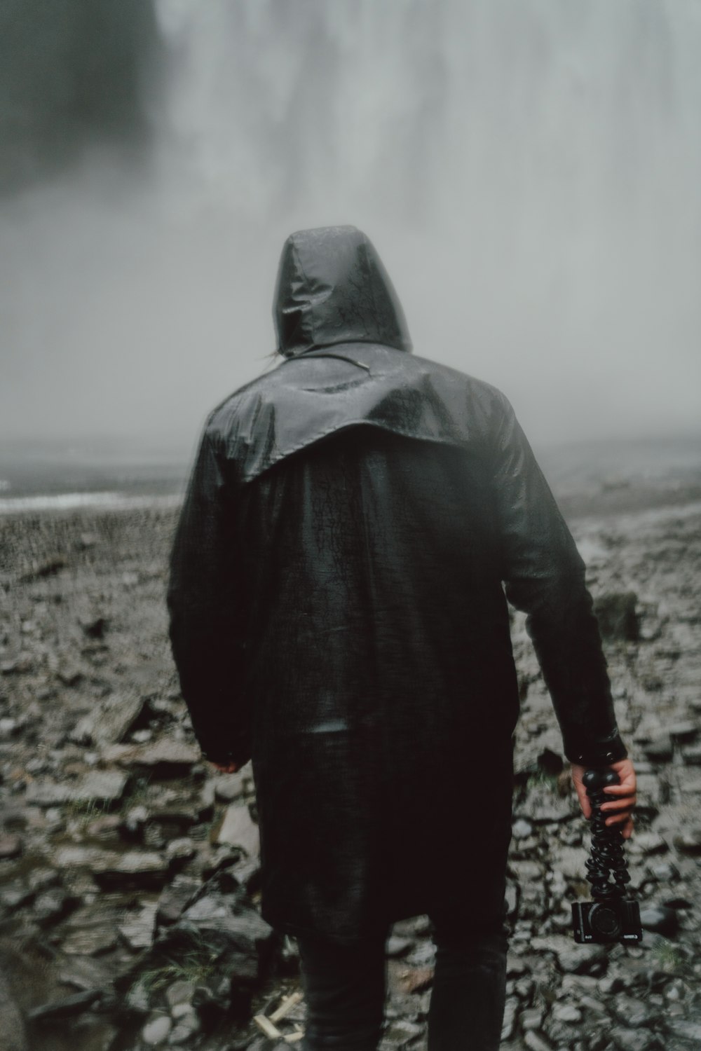 photography of man holding camera walking towards waterfalls during daytime