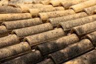 Rows of rustic terracotta roof tiles are closely aligned, featuring a weathered and textured surface with earthy tones and speckles.