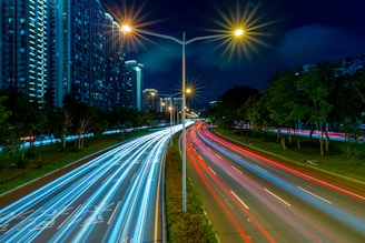 timelapse photography of vehicle tailights in street with lighted post beside buildings at daytime