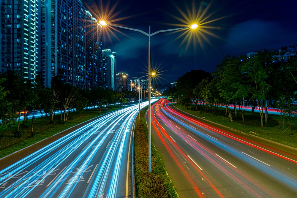 timelapse photography of vehicle tailights in street with lighted post beside buildings at daytime