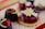 A close-up view of an assortment of artisanal desserts, including a cookie topped with a glossy berry glaze and an edible flower, alongside colorful, marbled chocolates.