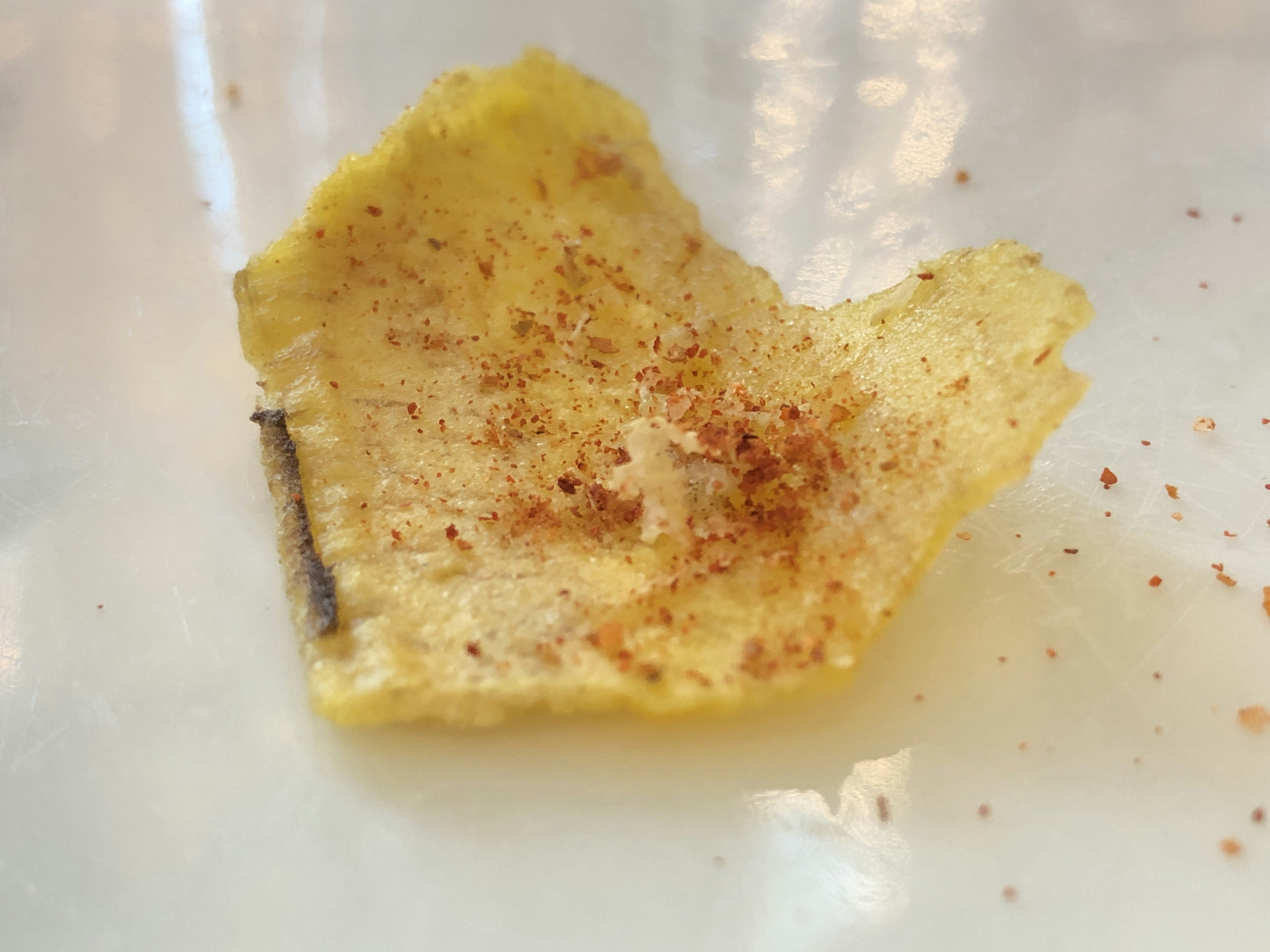 Keripik kentang kuning keemasan dengan bumbu merah balado tersebar di atas permukaan hitam dengan pencahayaan dramatis