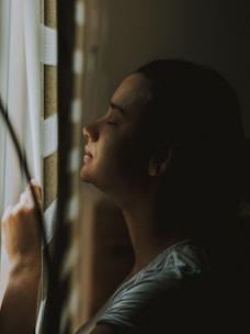 A serene morning scene with a woman gently cleansing her face by a sunlit window.