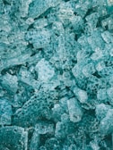 A close-up view of numerous irregularly shaped translucent blue ice cubes, clustered together with intricate patterns and textures.