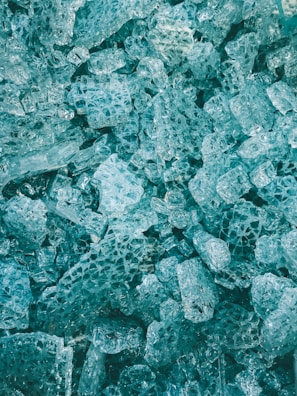A close-up view of numerous irregularly shaped translucent blue ice cubes, clustered together with intricate patterns and textures.
