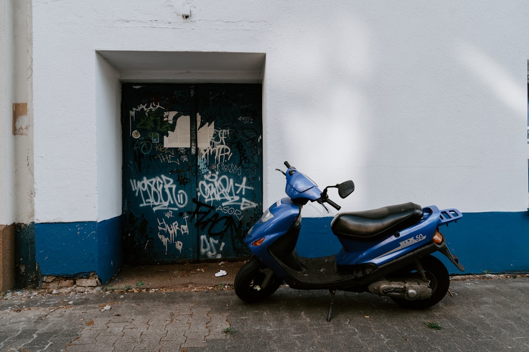 blue motor scooter parked in front of white and blue concrete wall with green gate