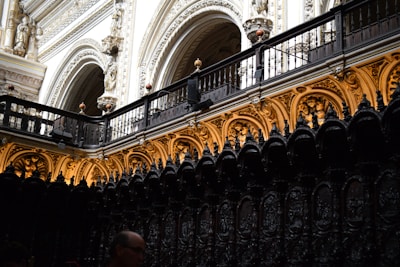 An intricately designed interior with high arched ceilings and ornate carvings. The upper section features elaborate architectural details with statues and decorative arches. The lower part of the image shows a dark, richly carved wooden structure.
