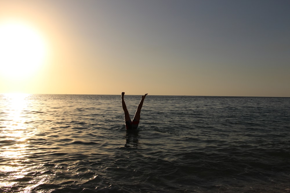 pessoa mostrando pernas no corpo de água durante o pôr do sol