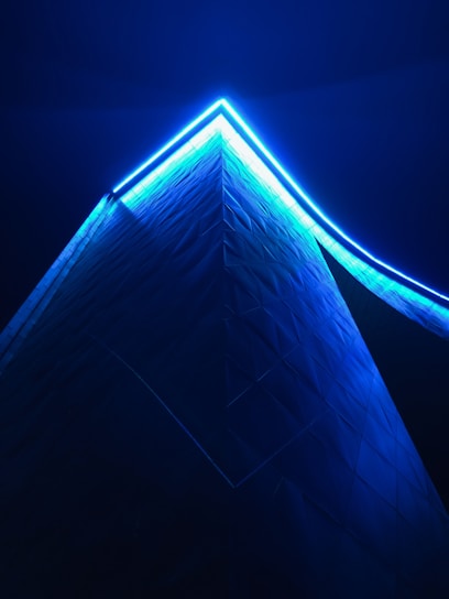 A sleek, abstract architectural structure illuminated with electric cyan accents against a deep space blue background.