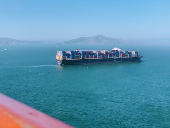 A modern cargo ship loaded with colorful shipping containers sailing under a clear blue sky.