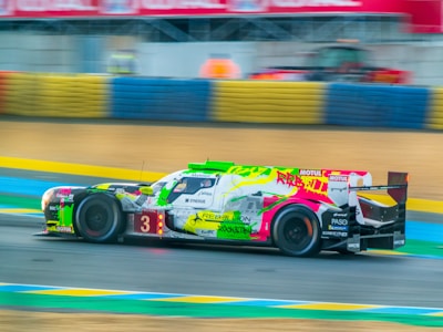 A racing car with vibrant graffiti-style art on its body zooms along a race track. The background includes colorful barriers and blurred elements, indicating motion and speed.