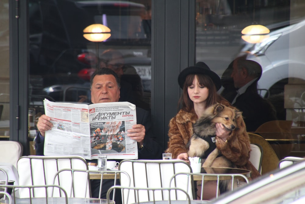 man holding newspaper article sitting beside woman holding dog