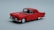 A miniature model of a classic red car with a glossy finish, showcasing intricate details such as the chrome front bumper, headlights, and wheels against a plain gray background.