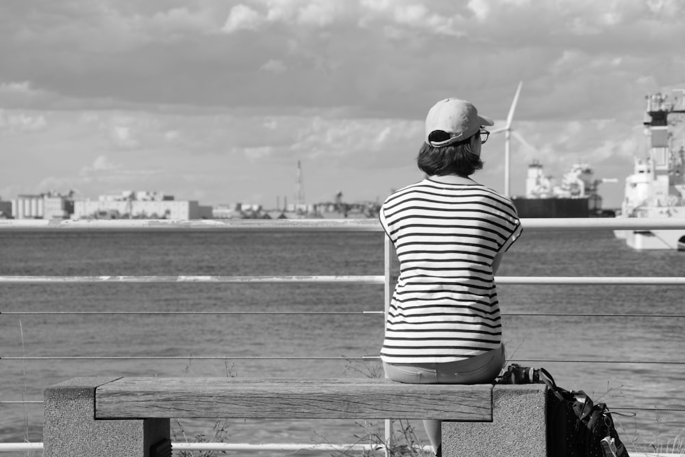 grayscale photo of woman sitting on bench facing sea