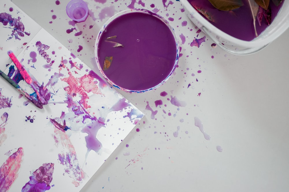 a cup of purple paint next to a paintbrush