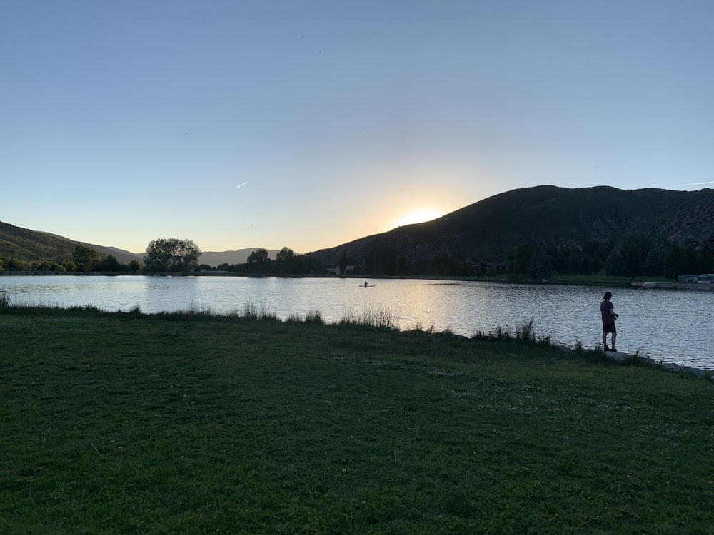 person standing on green grass near body of water