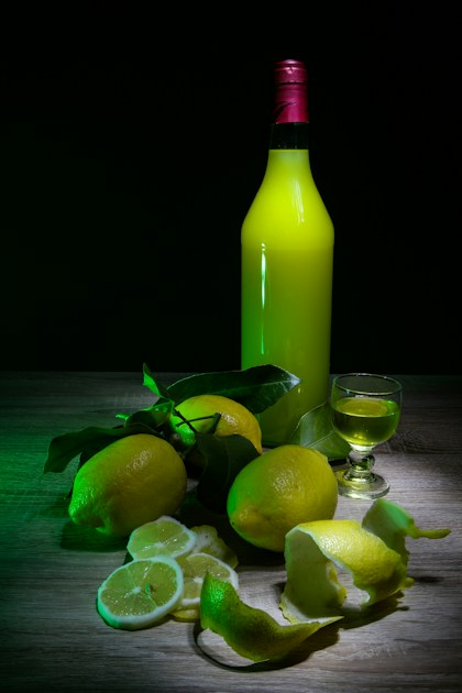 Bouteille de limoncello artisanal entourée de citrons frais et petit verre de dégustation