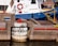 A dock area with a blue and white boat named Ned Hanlan II is tied with yellow ropes. The dock features concrete structures with red bollards, and a stack of worn tires serves as a fender. Cables and a life buoy are visible on the boat.