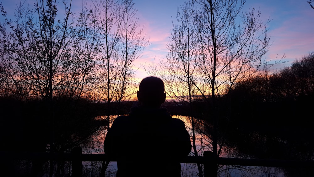 silhouette of man watching orange setting sun in horizon