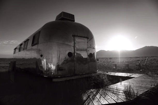 Sleek black and silver travel trailer parked on a scenic mountain overlook at sunset.