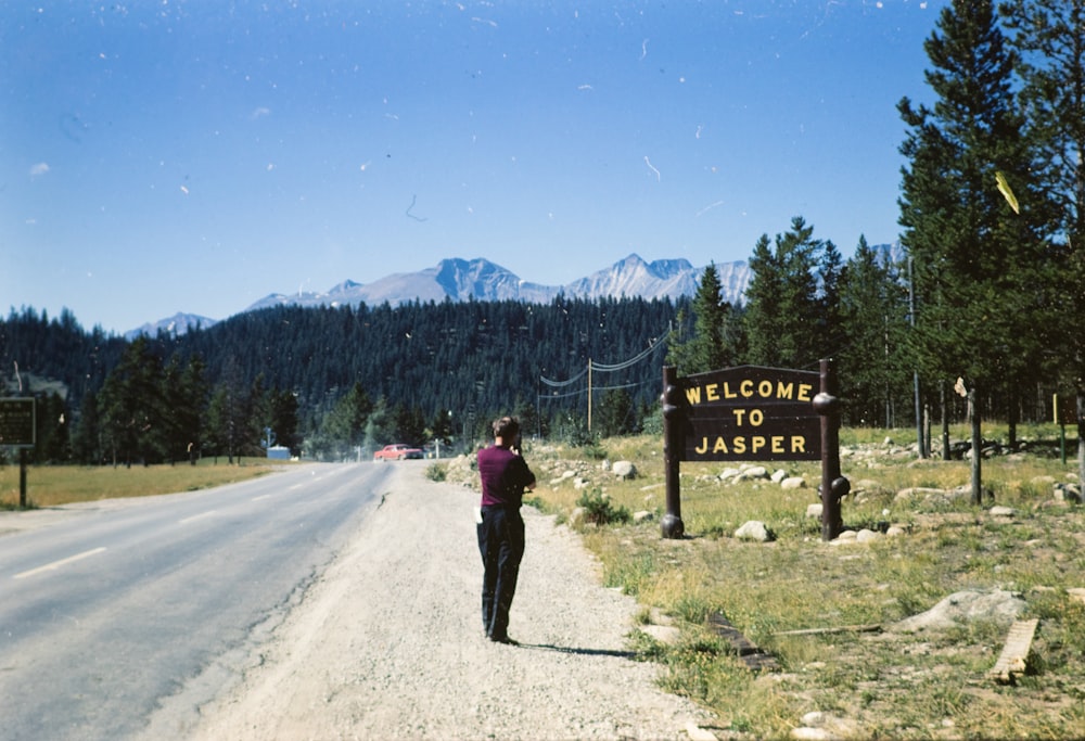 man man beside road in front of welcome to jasper signage during daytime