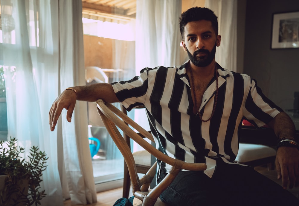 man wearing black and white striped dress shirt sitting on chair]