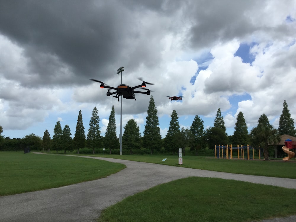two black quadcopter drones hovering over green grass field