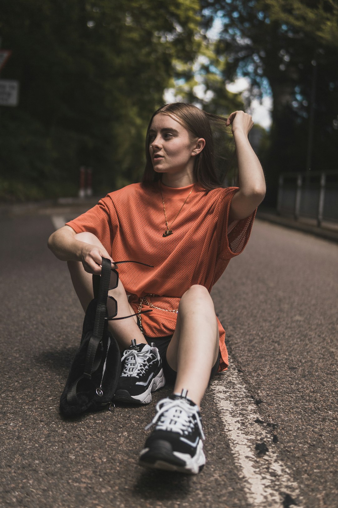 woman sitting on road between trees